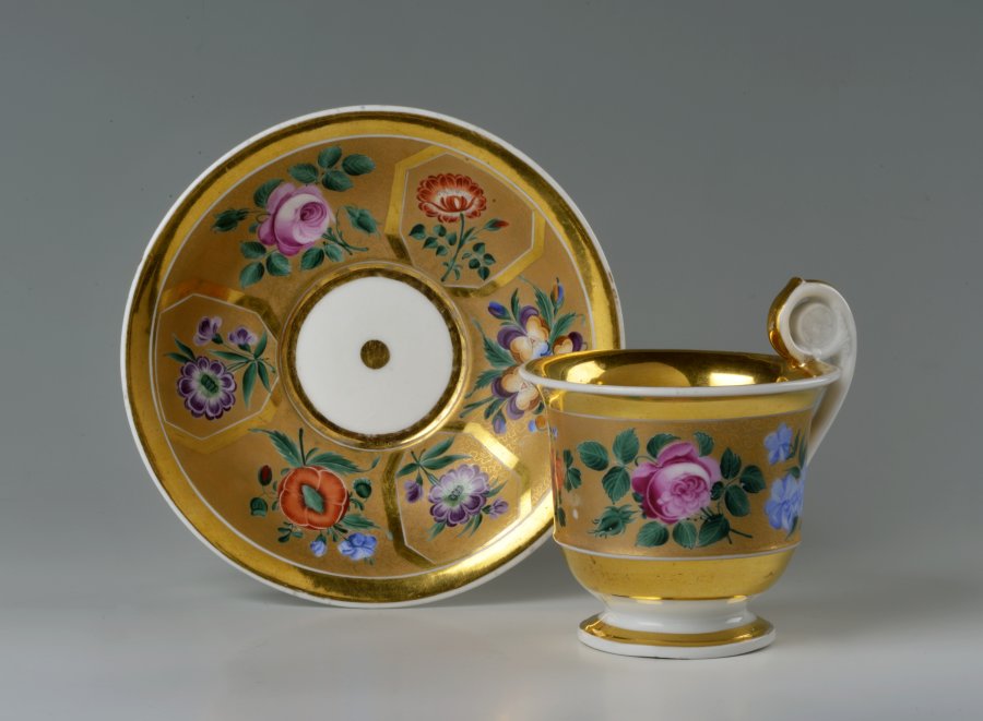 A CUP AND SAUCER WITH A FLORAL DECORATION